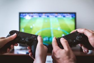 Image of two hands holding game console infront of tv screen.